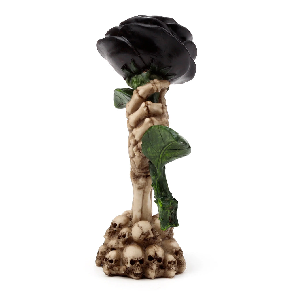 Angled view of a Gothic-style ornament, showing a bone-coloured skeleton hand holding a large black rose with green leaves, atop a base of stacked skulls.