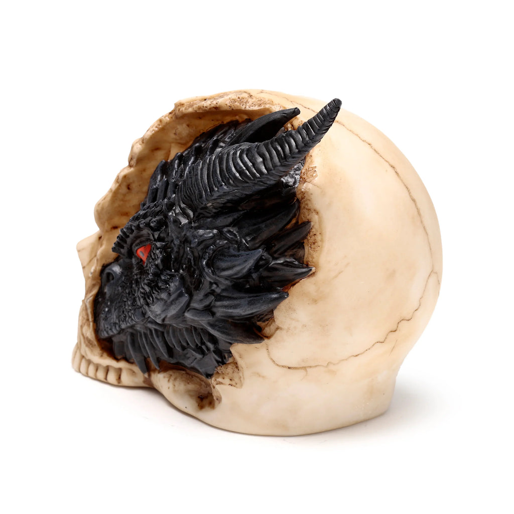 Figurine of a black dragon's head, featuring red eyes, ridged horns, and textured scales, dramatically emerging from a cracked, light-coloured human skull, shown from an angled perspective on a white background.