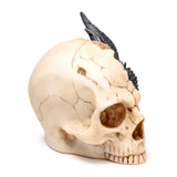 Angled view of a large ornamental beige skull figurine, detailed with dark cracks and featuring textured black dragon scales and spikes emerging from the top.