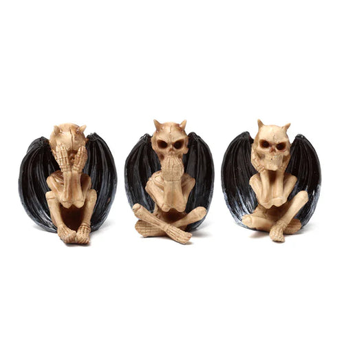 Front view of three bone-coloured skeletal winged demon ornaments, each depicting one of the 'see no evil, speak no evil, hear no evil' poses, with large black wings and small horns.