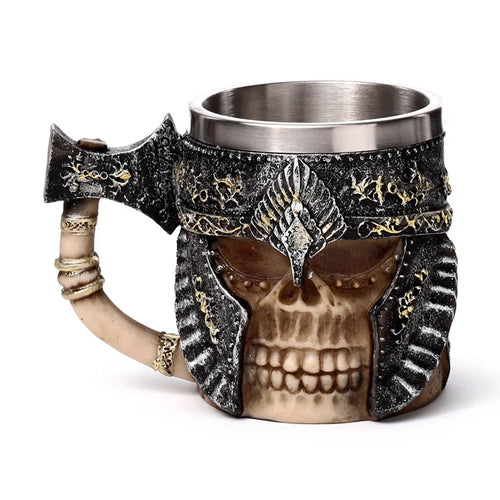 Angled view of a decorative tankard, featuring a bone-coloured armoured skull with dark, textured armour and gold detailing. The handle is shaped like an axe, with bone-like rings. It has a silver metallic inner cup.