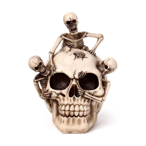 Front view of a decorative cream skull ornament, featuring three small skeletons appearing to burst from and climb its distressed, textured surface.