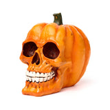 Angled view of an orange decorative pumpkin skull ornament, featuring hollow eye sockets, a nose cavity, white teeth, and a green stem.