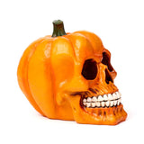 Orange decorative pumpkin skull ornament. Angled view showing dark eye sockets, a deep nose cavity, bared white teeth, and a green stem.