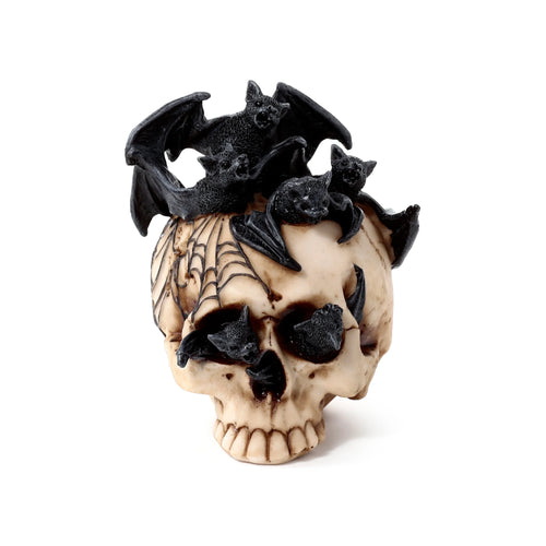 Angled view of a decorative beige-coloured skull ornament, featuring black bats emerging from its eye sockets and mouth, with a black spiderweb detail on the side.
