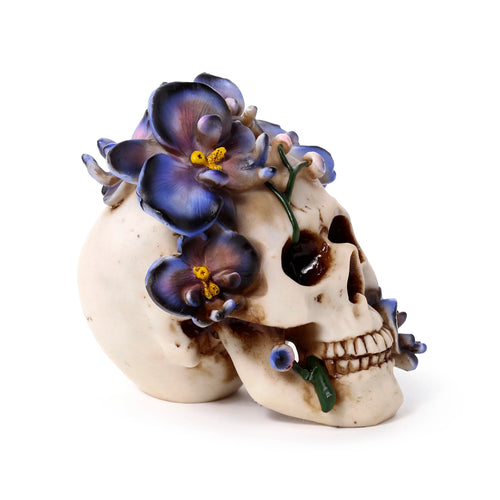 Angled view of a cream-coloured skull decorative ornament, adorned with purple vine flowers and green stems.