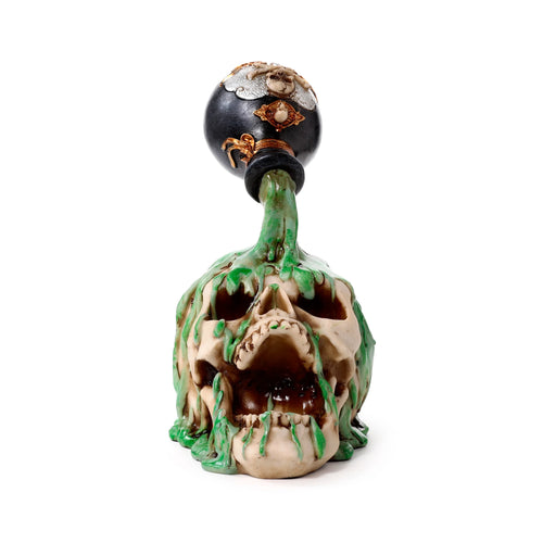 Front view of a decorative bone-coloured screaming skull ornament with green slime dripping from its eye sockets and mouth, topped by a black ornate bottle featuring gold and silver detailing.