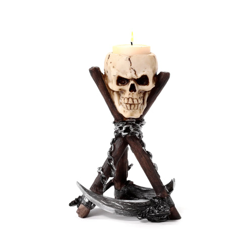 Front view of a cream-coloured skull tea light holder with dark eye sockets and cracks, holding a lit candle. It stands on a dark brown and silver scythe tripod base with silver chain details.