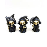 Front view of three decorative mini reaper skull figurines, each wearing a black hooded robe and holding a scythe, presented on a white background.