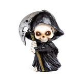 Angled view of a decorative reaper mini skull ornament, featuring a skull head with dark eye sockets, a black hooded robe, and holding a silver-bladed scythe, set against a white background.