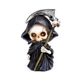 Front view of a decorative miniature grim reaper figurine with a white skull face and dark eye sockets, wearing a black hooded cloak and holding a silver scythe adorned with a small skull.