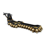 Angled view of a decorative Grim Reaper Death Cross incense burner. The black, cross-shaped burner features a hooded Reaper figure holding a scythe at one end, with numerous golden skull heads lining its edges and intricate golden patterns inside the tray.
