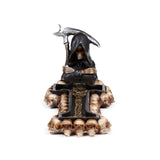 Front view of a Decorative Incense Burner, depicting a Grim Reaper in a black hooded robe holding a scythe, seated on a dark, cross-shaped base adorned with multiple skulls and a golden intricate pattern.