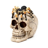 Angled view of a decorative cream-coloured skull ornament with dark markings, topped by a black and orange hairy spider.