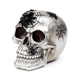 Angled view of a textured silver skull ornament, adorned with black spiders and spider webs.