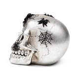 Textured silver skull ornament in left profile, decorated with black spiders and webs.