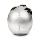 Back view of a textured silver skull ornament, adorned with multiple black spiders and featuring a visible vertical suture line.