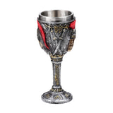Full view of a decorative goblet, featuring a metallic silver finish with gold accents. The bowl displays intricate details including crossed swords, a red plume design, and a visible skull motif, all above a detailed stem and base.