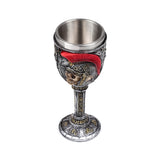 Angled view of a decorative Roman soldier goblet, featuring a skull wearing a helmet with a red plume. The goblet has a metallic grey finish with gold-coloured intricate patterns and a silver-coloured inner cup.