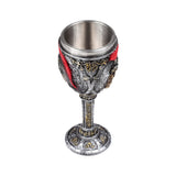 Angled overhead view of a decorative goblet, featuring a metallic inner cup, a distressed silver exterior with gold accents and red elements, and intricate carvings depicting Roman soldier armour.