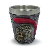 Front view of a decorative shot glass, depicting a Roman soldier's helmet with a prominent red plume and a skull design, in silver, grey, and gold colours.
