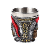 Angled view of a decorative Roman soldier themed shot glass, featuring a silver-coloured outer with gold scrollwork, red plume details, and a visible skull motif.