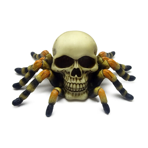 Front view of a decorative skull ornament with a creamy bone finish and eight splayed orangey-brown and black segmented spider legs.