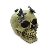 Angled view of a pale bone-coloured skull decorative ornament, adorned with intricate metallic grey butterflies on its top and side.