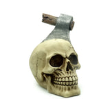 Decorative skull ornament, angled view showing a pale, cracked skull with an embedded metallic axe and weathered wooden handle.