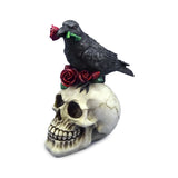 Angled view of a decorative ornament featuring a detailed, off-white skull with a black raven perched on its top, holding a red rose in its beak, and surrounded by several red roses.