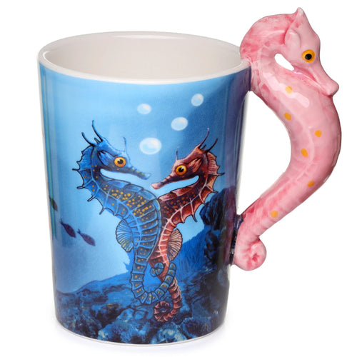 Angled view of a ceramic mug with a pink seahorse-shaped handle, depicting an underwater scene with two detailed seahorses, one blue and one reddish-brown, on a light blue background with fish and bubbles.