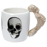 Angled view of a white ceramic mug featuring a black and white skull graphic and a sculpted beige skeleton handle.