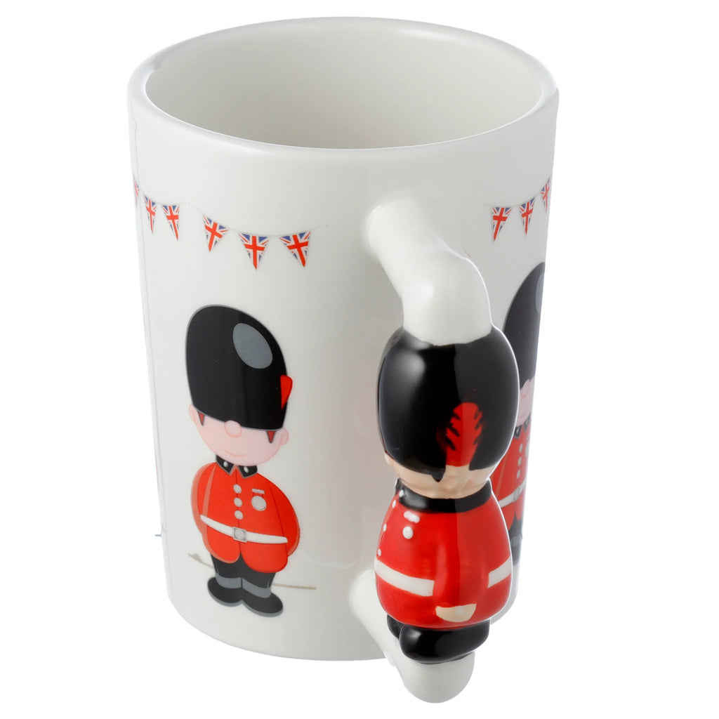 Angled view of a white ceramic mug with a Guardsman figure shaped handle, decorated with cartoon Guardsmen in red uniforms and Union Jack bunting print.