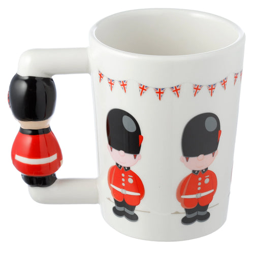 Angled view of a white ceramic mug with a shaped Guardsman figure handle and printed cartoon Guardsmen wearing red tunics below Union Jack bunting.