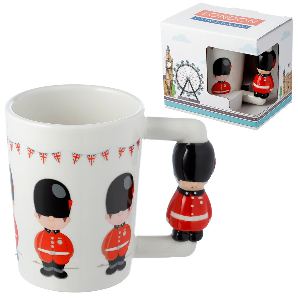 Angled view of a white ceramic Guardsman figure shaped handle mug, featuring cartoon Guardsmen and Union Jack bunting, with its product packaging visible in the background.