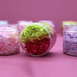 Angled view of a clear plastic jar of Strawberry & Kiwi whipped soap, lying on its side, showing vibrant lime green and deep reddish-pink textured layers.