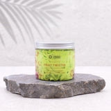 Front view of a clear jar of light green strawberry and kiwi whipped soap with a silver lid, presented on a grey stone slab.