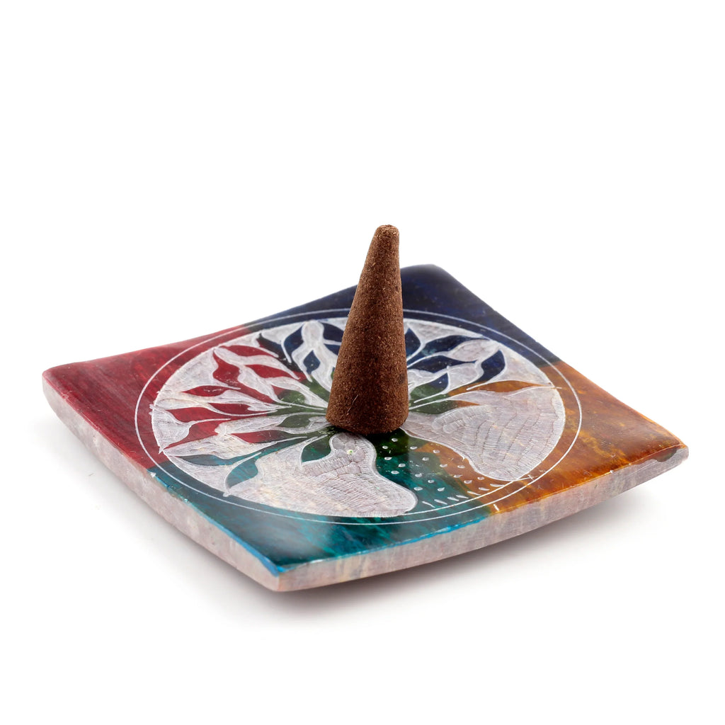 Angled view of a colourful soapstone incense burner dish with a carved Tree of Life design and a brown incense cone.