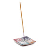 Angled view of a multi-coloured soapstone incense burner dish, featuring an engraved Tree of Life design on its surface, with a brown incense stick upright in the centre.