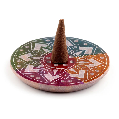Angled view of a multi-coloured soapstone incense burner dish, featuring an engraved white sunburst mandala pattern, multiple holes, and a brown incense cone placed centrally.