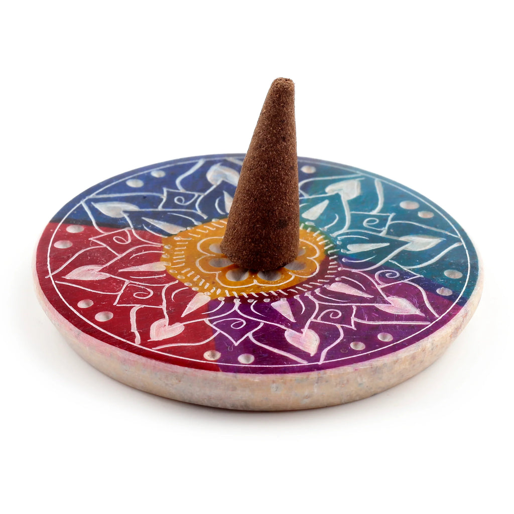Angled view of a round, colourful soapstone incense burner dish featuring intricate flower petal and mandala patterns in red, purple, blue, and yellow, with a brown incense cone standing centrally.