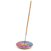 Angled view showing a colourful round soapstone incense burner dish with an intricate carved flower petal design, holding an unlit incense stick.