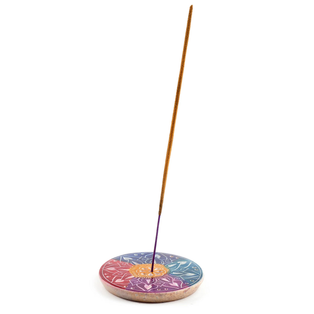 Angled view showing a colourful round soapstone incense burner dish with an intricate carved flower petal design, holding an unlit incense stick.