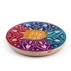 Angled view of a round, multi-coloured soapstone incense burner dish on a white background, featuring an engraved flower petal mandala design in a rainbow spectrum of red, orange, purple, blue, and teal, with small circular holes for incense sticks.