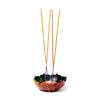 Carved soapstone chakra lotus incense burner dish, featuring vibrant multi-coloured petals. Four natural-coloured incense sticks with purple bases are visible, standing upright in the holder.