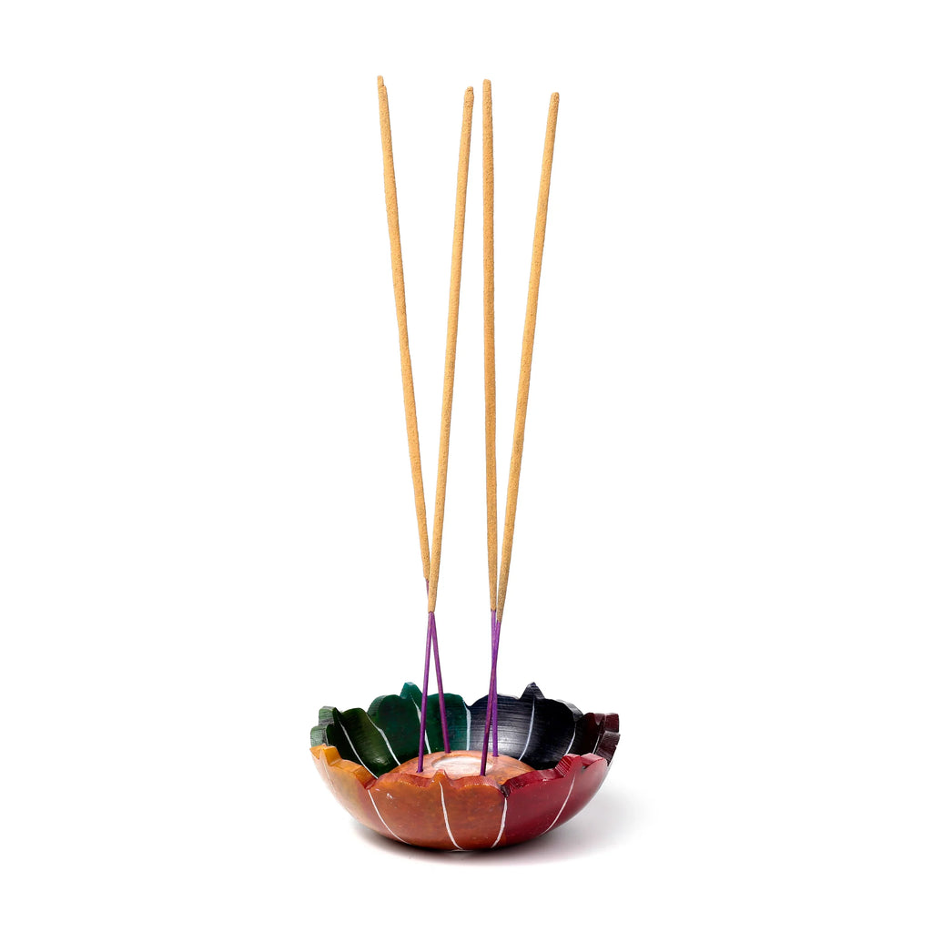 Carved soapstone chakra lotus incense burner dish, featuring vibrant multi-coloured petals. Four natural-coloured incense sticks with purple bases are visible, standing upright in the holder.