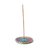 Round carved soapstone incense burner dish, showcasing a rainbow-coloured chakra lotus design, with an upright incense stick, on a white background.