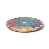Angled view of a round, carved soapstone incense burner dish, displaying a vibrant, multi-coloured chakra lotus design on its top surface with a central hole.