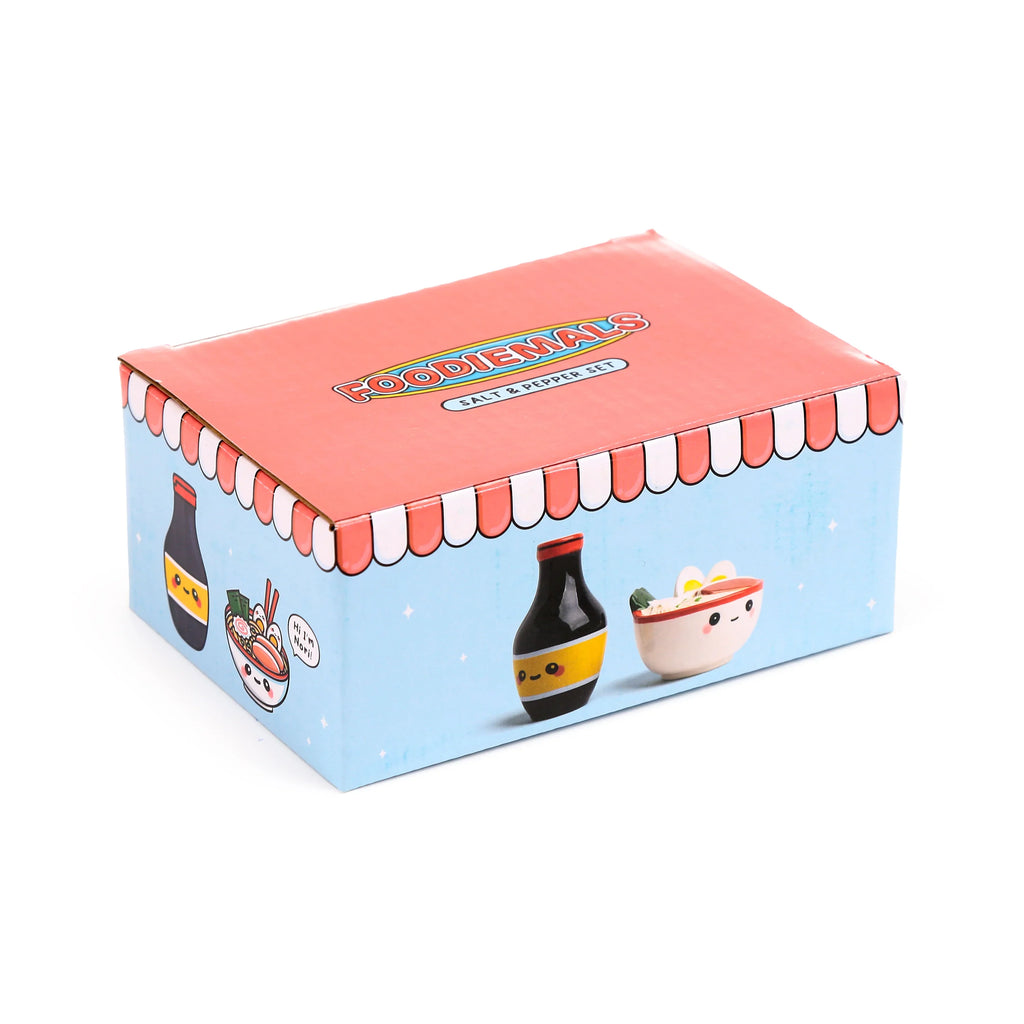 Angled view of the ceramic salt and pepper set packaging. The red-topped, light blue box features Foodiemals Salt & Pepper Set text, a scalloped border, and cartoon illustrations of a ramen bowl and soy sauce bottle with faces.