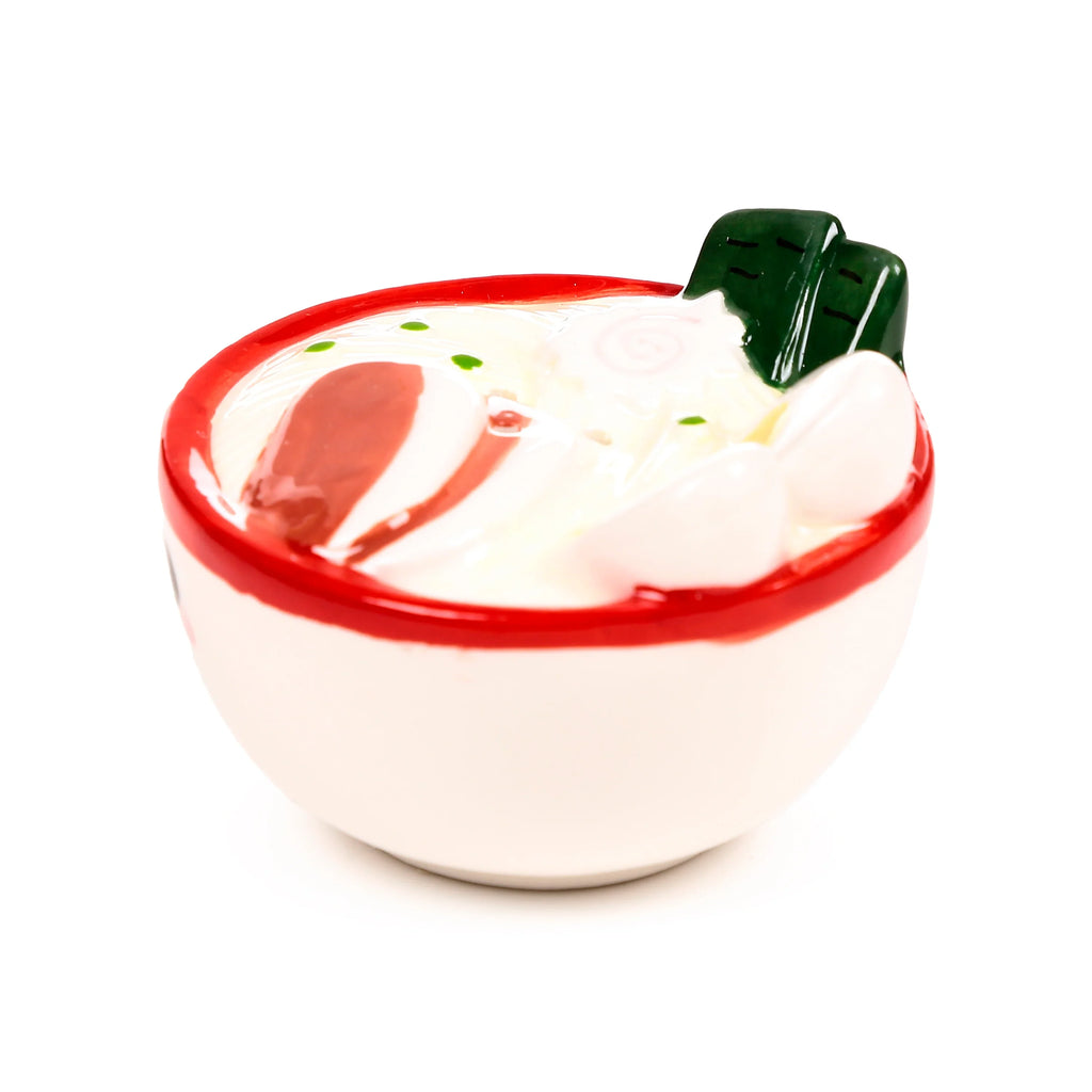 Angled view of a ceramic ramen bowl salt or pepper shaker with a red rim, featuring white noodles, red pork slices, green spring onions, pink narutomaki, and dark green nori seaweed.